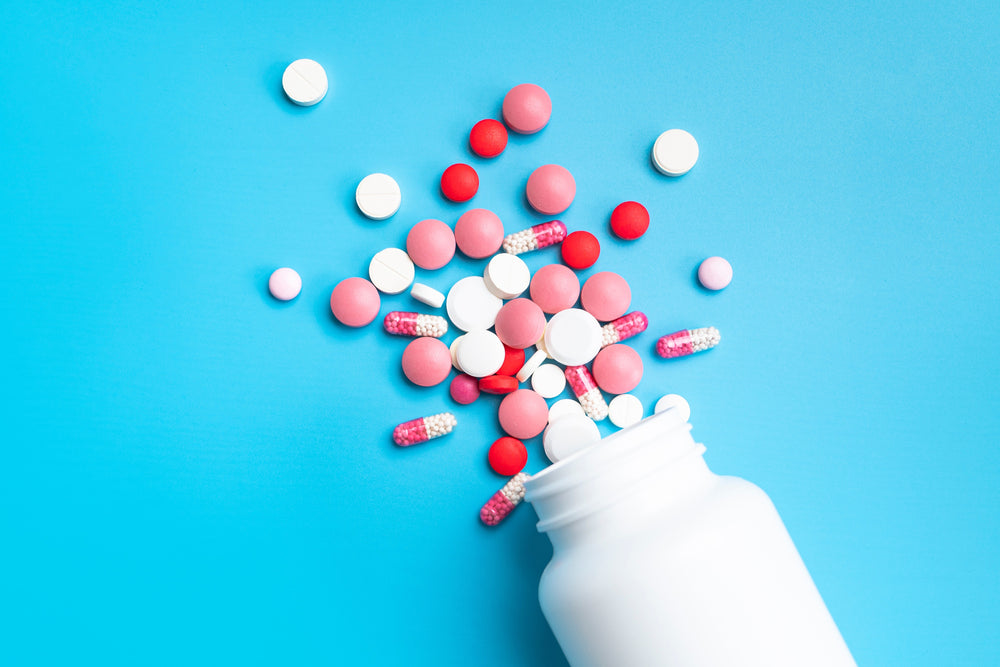 A mix of red, pink, and white pills spill from a bottle on a blue background.