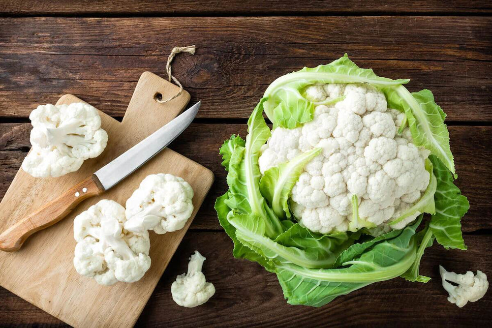 Two cut cauliflower florets sit on a cutting board next to a whole head of cauliflower.