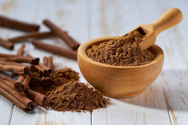 A bowl of powdered cinnamon sits next to a pile of cinnamon sticks.