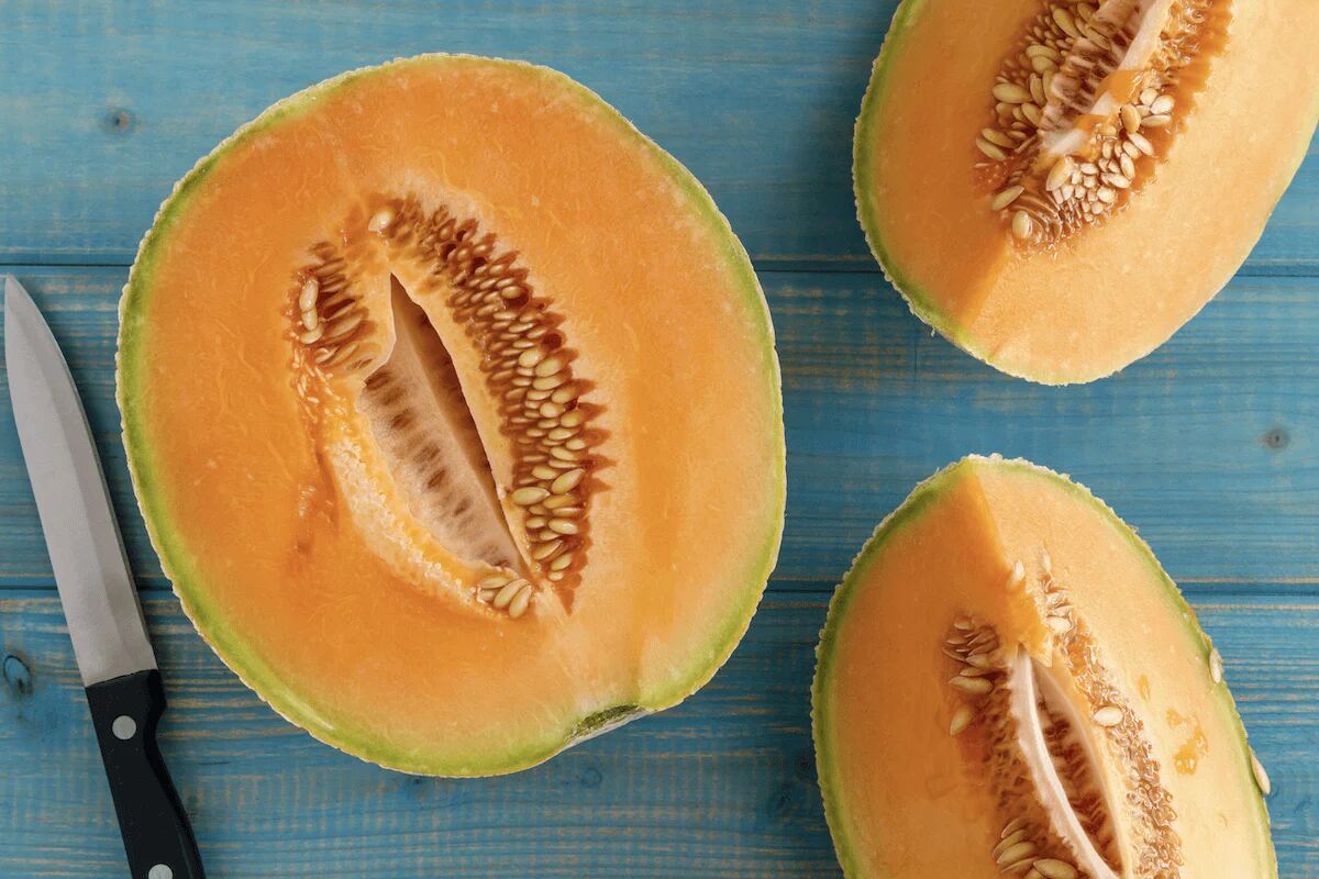 A sliced Cantaloupe sits on a blue wooden table.