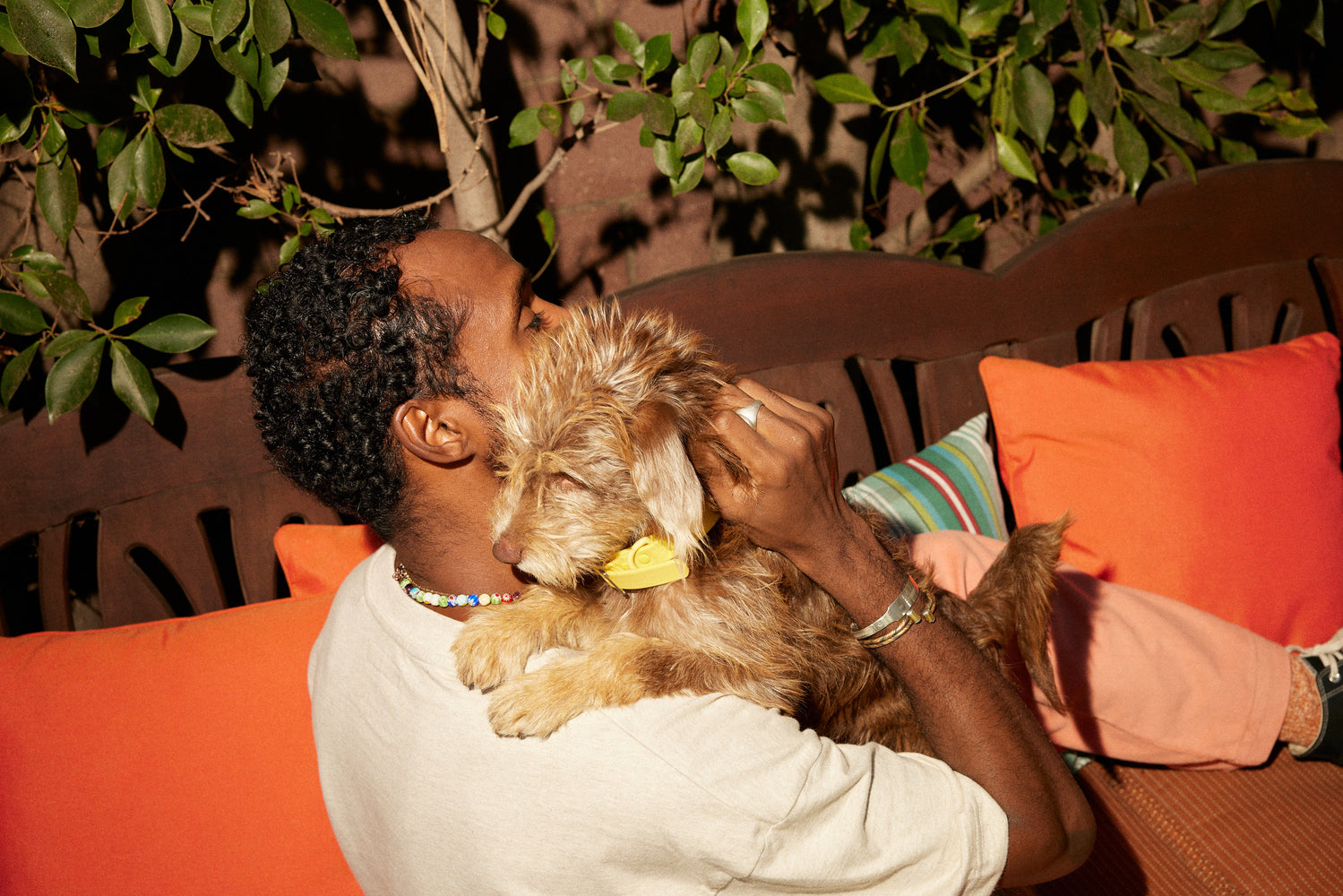 A man lounging on patio furniture hugs his small, furry dog.