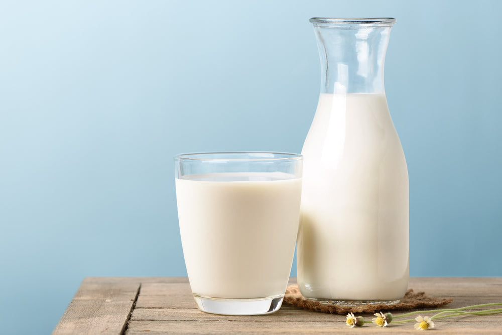 A glass and jug of milk sit on a wooden surface.