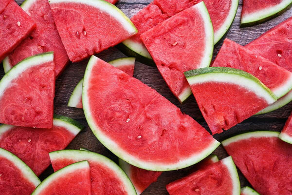 A pile of sliced watermelon sits on a black wooden surface.