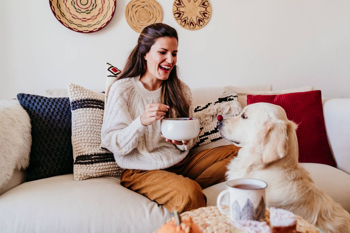 A woman laughs as she feeds her dog raspberries.